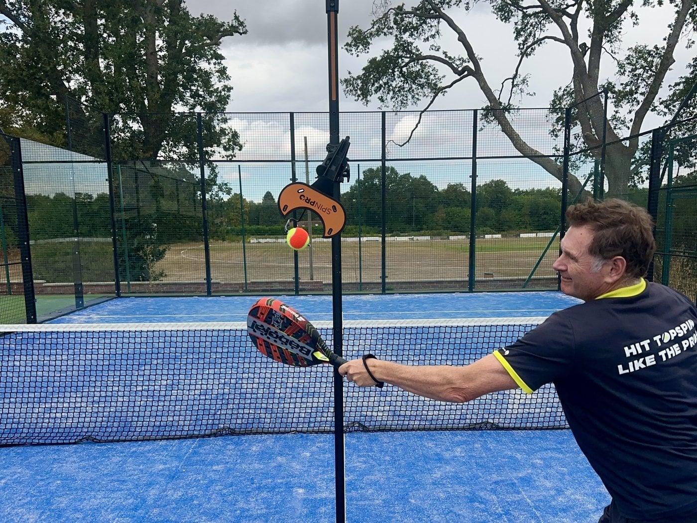 A padel player hitting repeated shots on the SpinPro beside the net