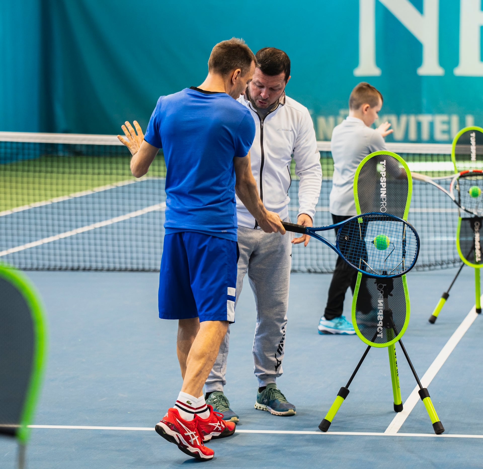 A coach demonstrating topspin to a junior using the TopspinPro